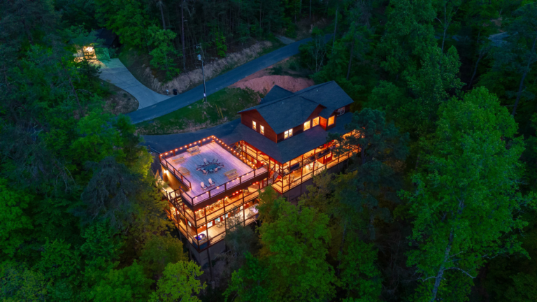 Large group cabin lit with string lights in a forested mountain setting.