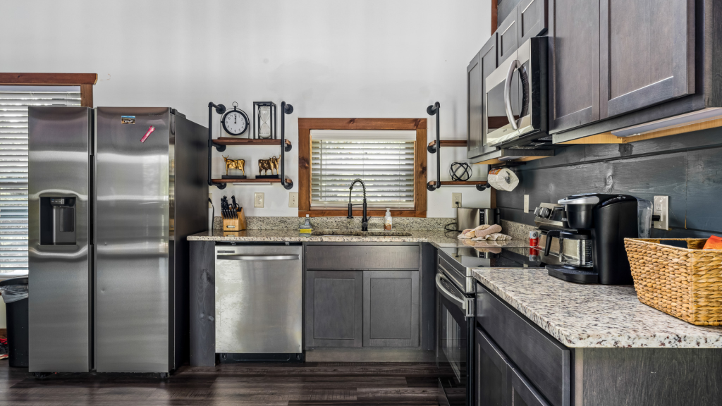 Clean cabin kitchen with stainless steel appliances, granite countertops, and industrial shelving, ready for guests.