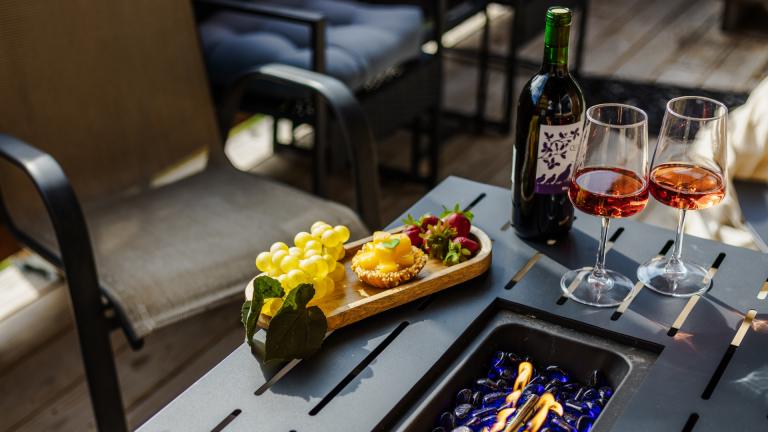 A cozy outdoor setup featuring wine glasses, fresh fruit, and a fire pit, perfect for romantic getaways.