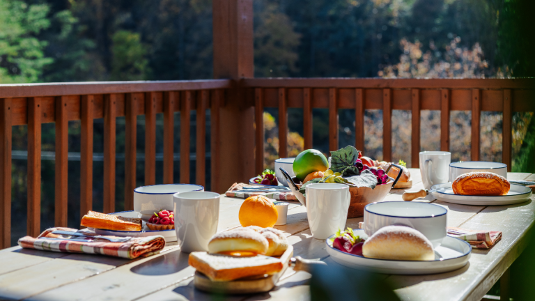 Romantic dining setup on a cabin deck with mountain views, fresh fruit, and pastries.