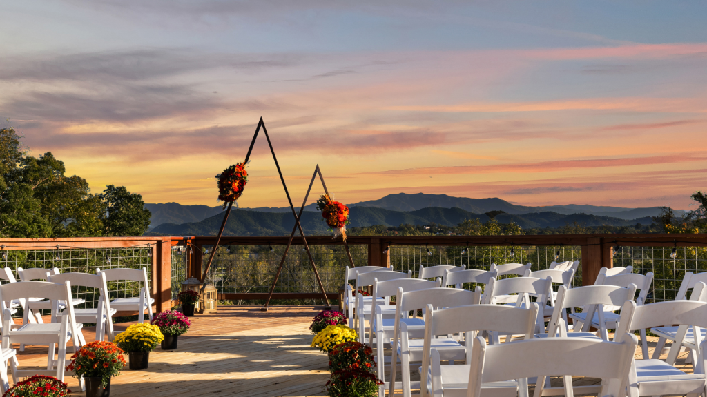 Outdoor Smoky Mountain wedding venue with a decorated ceremony arch, white chairs, and mountain views at sunset.