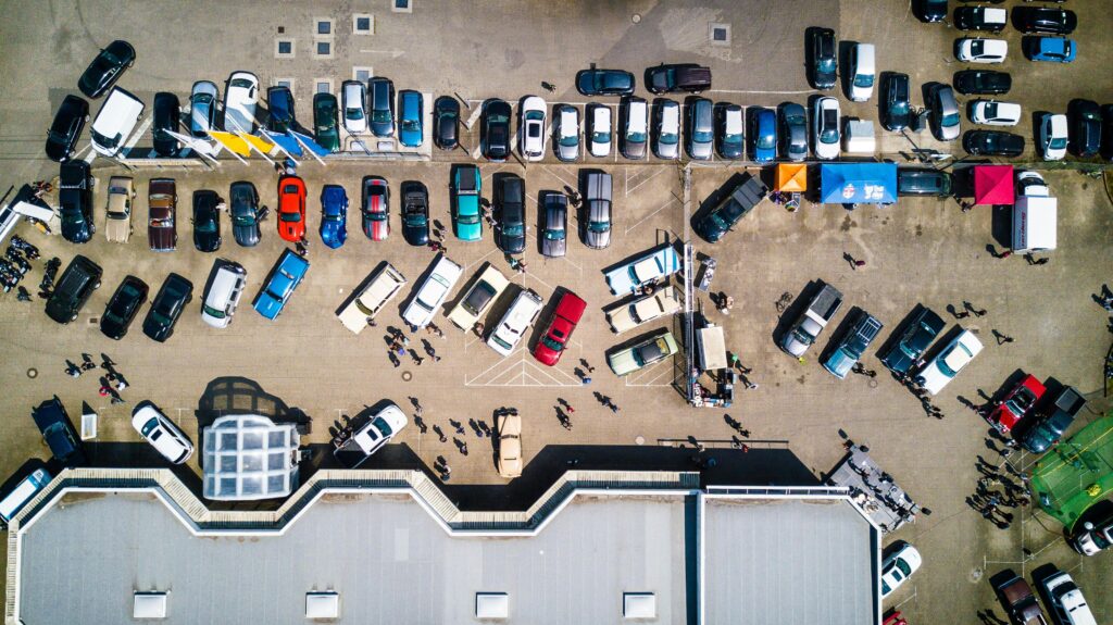 Aerial view of a busy parking lot filled with cars and trucks, with people walking between vehicles. Some tents and stalls suggest a market or event, and a building is visible&mdash;ideal for those seeking free parking in Gatlinburg.