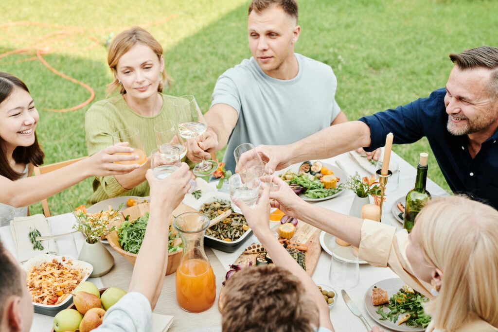 A group of people sitting around an outdoor table on a grassy lawn near Gatlinburg, raising their glasses for a toast. The table is filled with dishes and drinks, perfect after exploring Smoky Mountain waterfalls or hikes near Gatlinburg.