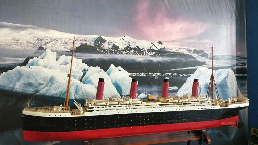 A large model of the Titanic ship is displayed at this popular Pigeon Forge attraction, set against a backdrop of icy waters, icebergs, and snow-covered mountains beneath a pink and purple sky—perfect for fans of the Titanic Museum.