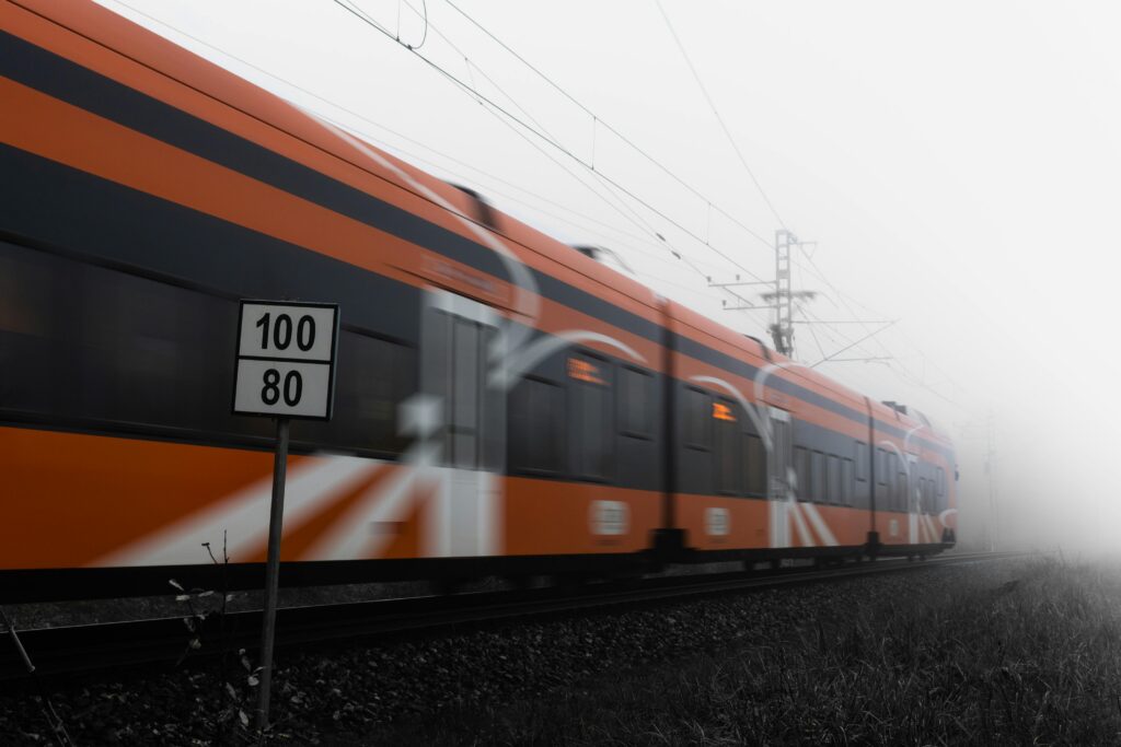 An orange train speeds past on railway tracks in a foggy setting, with a sign in the foreground displaying speed limits of 100 and 80—perfect inspiration for travel tips or things to do while exploring Gatlinburg in winter.