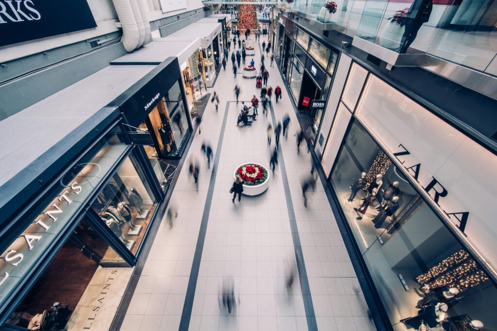 Aerial view of the busy Tanger Outlets Sevierville with blurred shoppers walking between store displays and clothing brand storefronts under bright lighting, perfect for vibrant shopping photos.