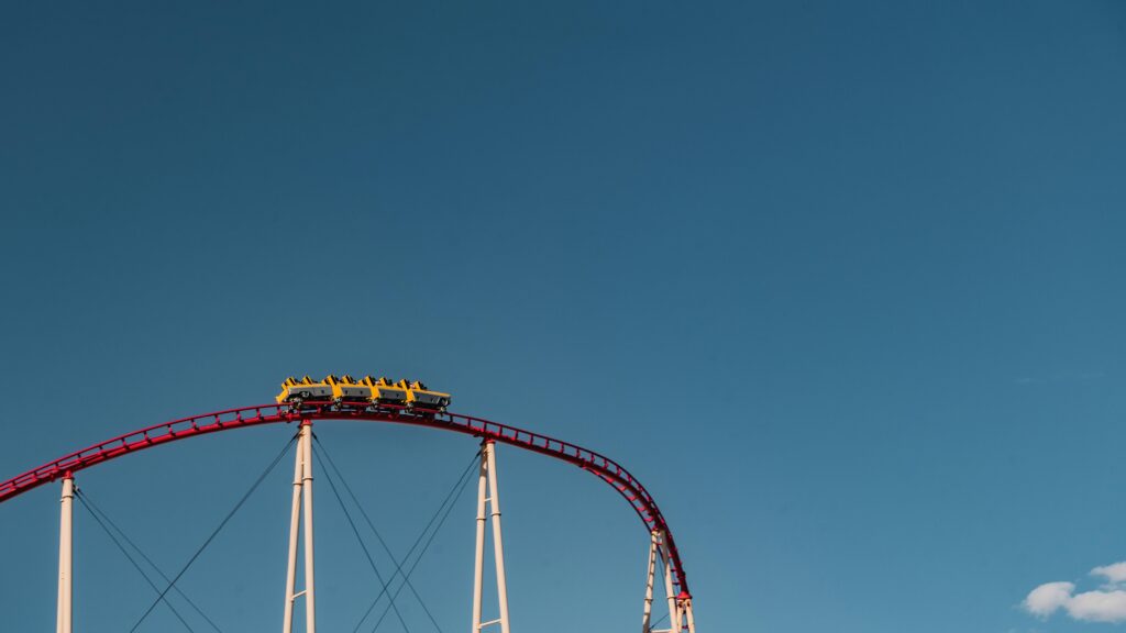 A thrilling roller coaster at Dollywood rides to the peak of a steep red track, its yellow cars poised against a clear blue sky and supported by sturdy white beams.
