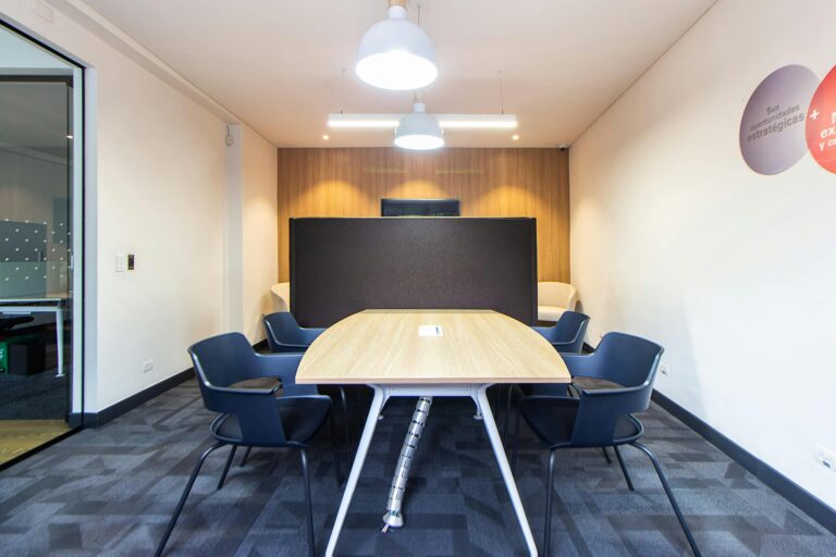 Modern meeting room perfect for corporate retreats or group events, featuring a wooden table, six black chairs, a black partition, white walls with wood paneling, gray carpet, and two ceiling lights. Ideal Meeting Spaces Gatlinburg location.