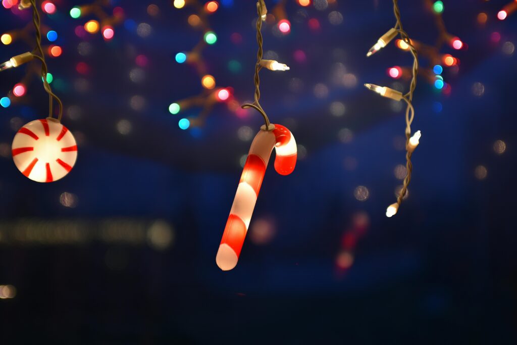 A glowing candy cane and peppermint light hang among multicolored string lights, creating a festive holiday atmosphere reminiscent of the best Christmas lights in Gatlinburg TN against a dark, blurry background.