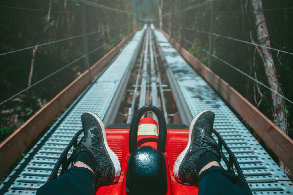 Riding a red alpine coaster down a metal track in the forest, with black sneakers visible and the track stretching ahead—experience one of the best mountain coasters in the Smoky Mountains.