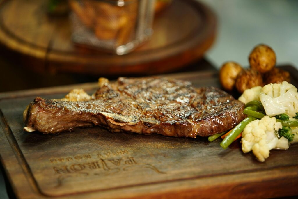 A grilled steak served on a wooden board with a side of mixed vegetables, including green beans, cauliflower, and mushrooms—just one highlight from the Cherokee Grill menu in Gatlinburg TN.