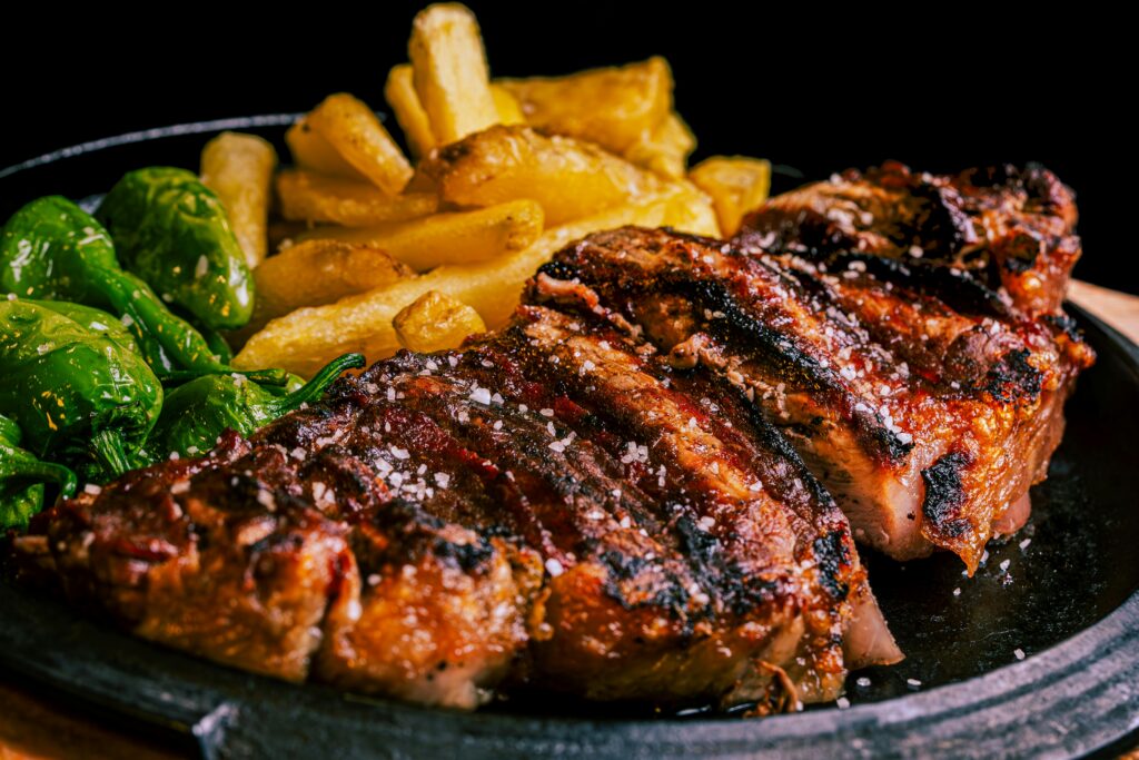 Grilled steak sliced and sprinkled with coarse salt, served with golden fries and green peppers—just like a signature dish at Greenbrier Restaurant in Gatlinburg—presented on a black plate against a dark background.
