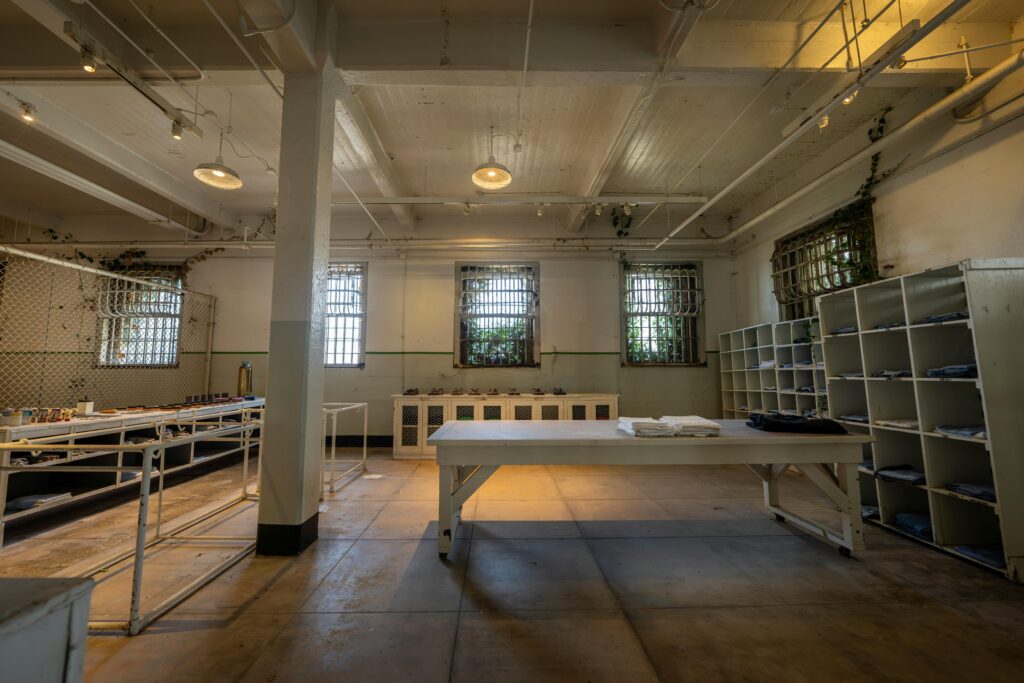Large, empty room with barred windows, metal shelving, and tables with folded linens—like a prison laundry at Alcatraz East Crime Museum in Pigeon Forge. Industrial lighting and worn floors complete the scene. Tickets available for tours.