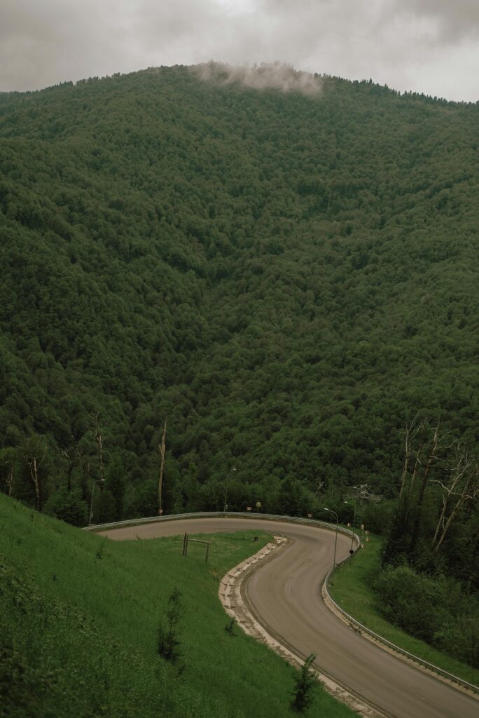 A winding road curves through lush green hillsides near Gatlinburg, offering scenic views as it leads toward a mountain covered in trees under a cloudy sky.