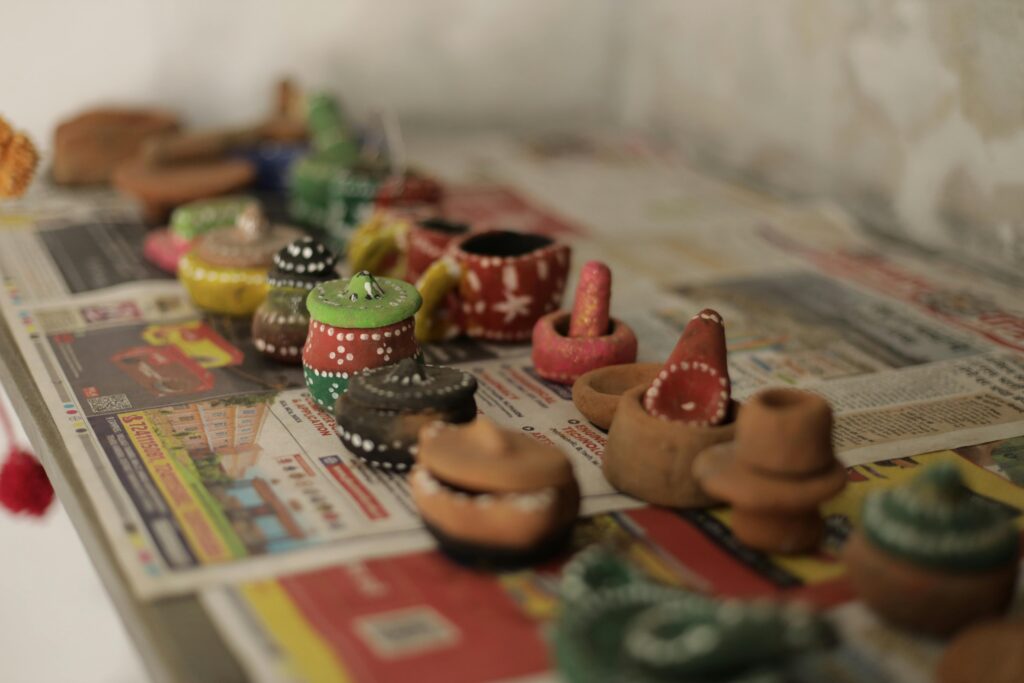 Small, hand-painted clay pots and vessels—showcasing the creativity of local crafts—sit atop colorful newspapers, arranged in rows. Each unique pot features vibrant colors and patterns, capturing the spirit of Gatlinburg Arts & Crafts handmade shops.