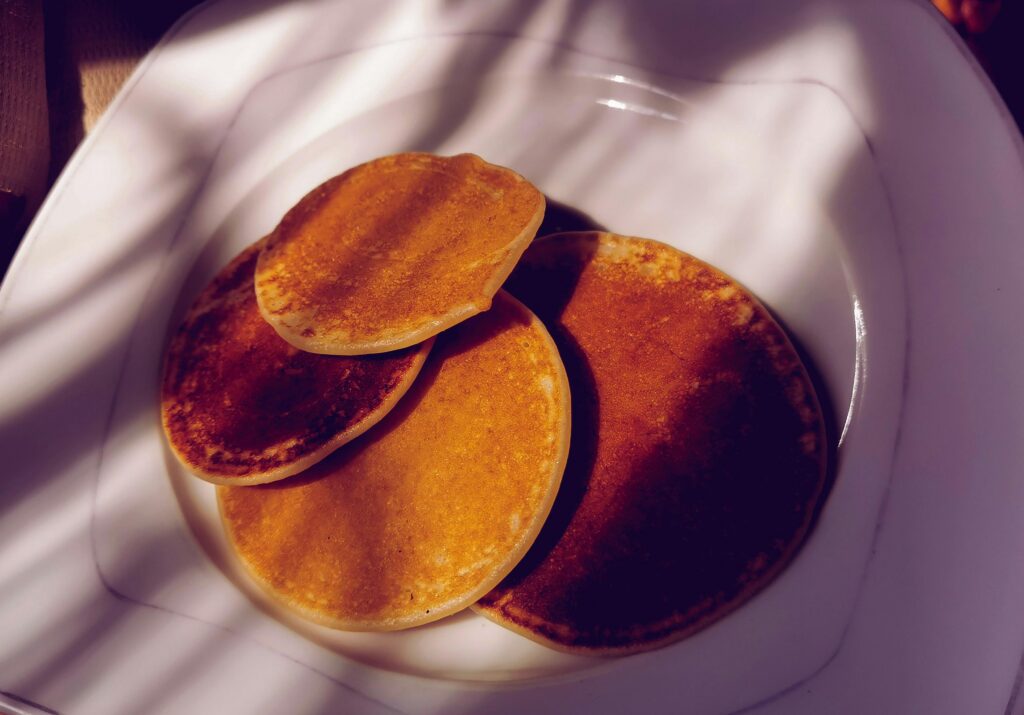 Four golden-brown pancakes are arranged slightly overlapping on a white plate, with shadows creating striped patterns&mdash;a mouthwatering example of what you might find at the best breakfast places in Gatlinburg.