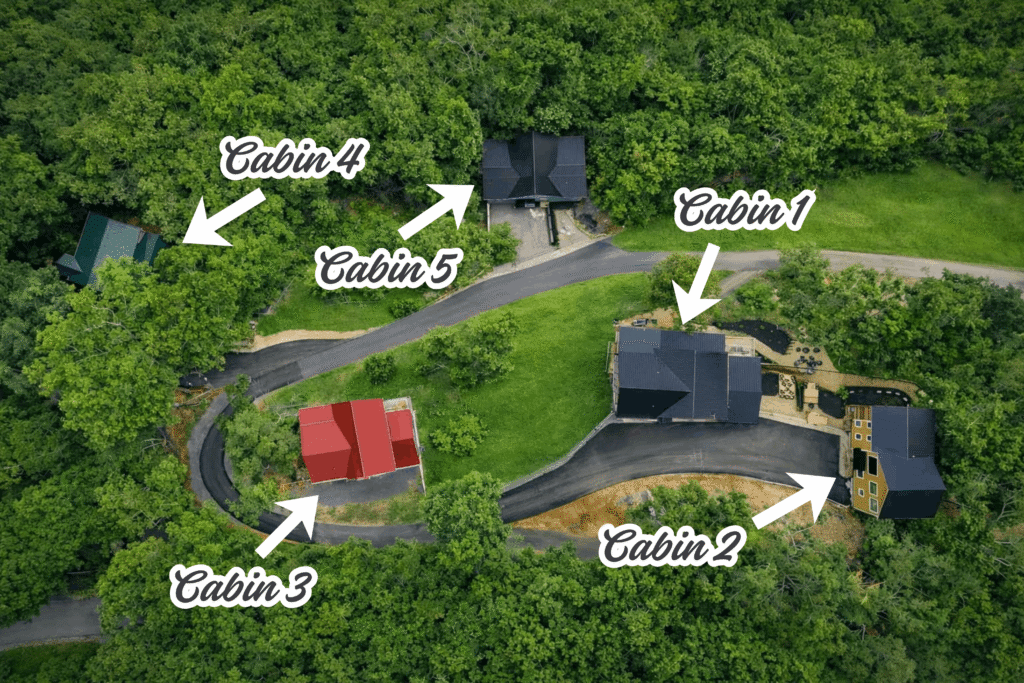Aerial view of five cabins labeled 1-5, surrounded by trees. Cabins are connected by paved roads. Cabins 1, 2, and 3 are near each other, while Cabins 4 and 5 are farther apart amid the woods.